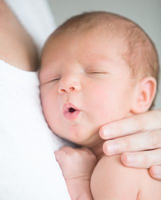 Portrait of a cute newborn hold at mother s breast Portrait of a cute newborn hold at mother s breast, his mouth open. Family, healthy birth concept photo, close up